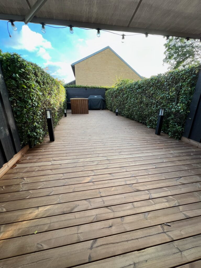 Træterrasse med hække og udendørs møbler