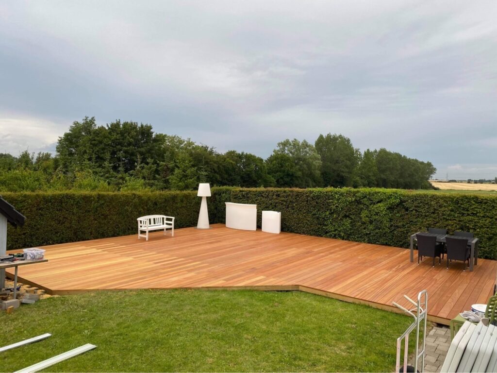 Stor træterrasse med havemøbler og grøn hæk
