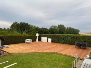 Stor træterrasse med havemøbler og grøn hæk